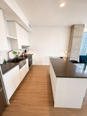 A modern kitchen with white cabinetry, a black countertop, and a wooden floor. - Spacious Deluxe 2BR - Perfect near Bayfront Park  Family Stay (Miami)