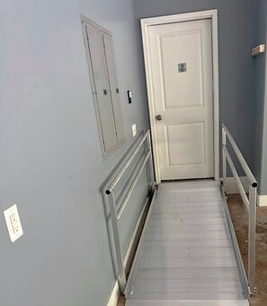 A narrow hallway with a door at the end, a light switch on the wall, and a metal handrail. - SASADEERLODGE 6-bedroom house with AC in Richmond Hill (Richmond Hill)