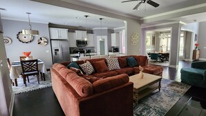 A modern living room with a brown sectional sofa, a coffee table, and a dining area with a table and chairs. - SASADEERLODGE 6-bedroom house with AC in Richmond Hill (Richmond Hill)