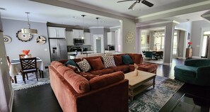A modern living room with a brown sectional sofa, a coffee table, and a dining area with a table and chairs. - SASADEERLODGE 6-bedroom house with AC in Richmond Hill (Richmond Hill)