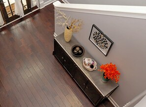 Een kamer met een donkere houten vloer, een witte muur en een zwarte console met decoratieve objecten.
