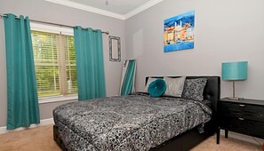 A bedroom with a bed, a nightstand, a lamp, a window with curtains, and a painting on the wall. - SASADEERLODGE 6-bedroom house with AC in Richmond Hill (Richmond Hill)
