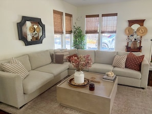 A living room with a beige sectional sofa, a coffee table with decorative items, and a large mirror with hats. - Superb 3-bedroom home in peaceful Atascadero (Atascadero)