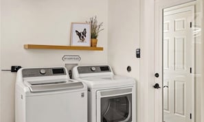 A laundry room with two white washing machines, a shelf with a framed picture, and a door. - Superb 3-bedroom home in peaceful Atascadero (Atascadero)