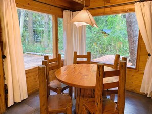 A wooden interior with a round table and chairs, large windows with curtains, and a hanging light fixture. - Cabañas en el bosque de Puerto Manzano (Puerto Manzano)