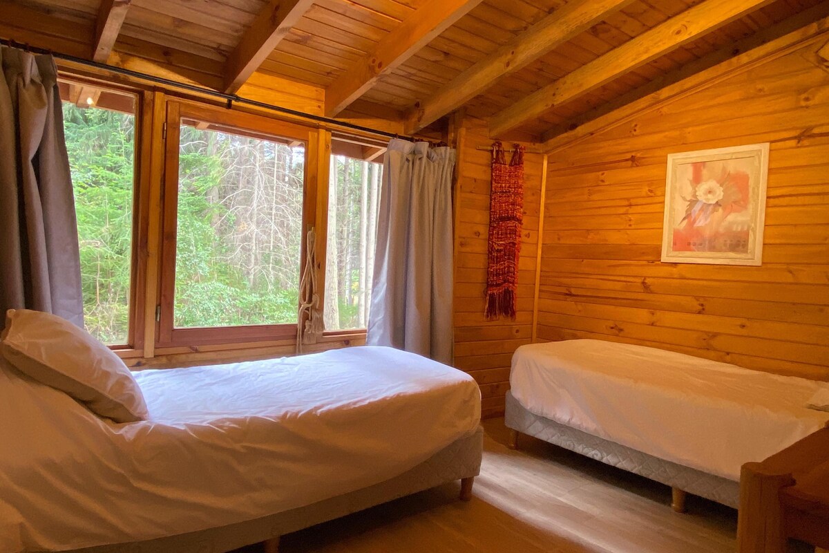 A cabin with two beds, wooden walls, and a window with curtains.