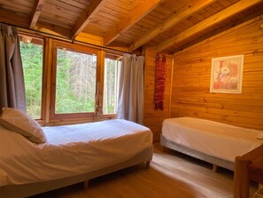 Uma cabana com duas camas, paredes de madeira e uma janela com cortinas.