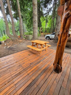 Um deck de madeira com uma mesa de piquenique, cercado por árvores.