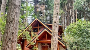 Una cabaña de troncos con base de piedra, rodeada de árboles y una escalera de madera que conduce a la entrada.