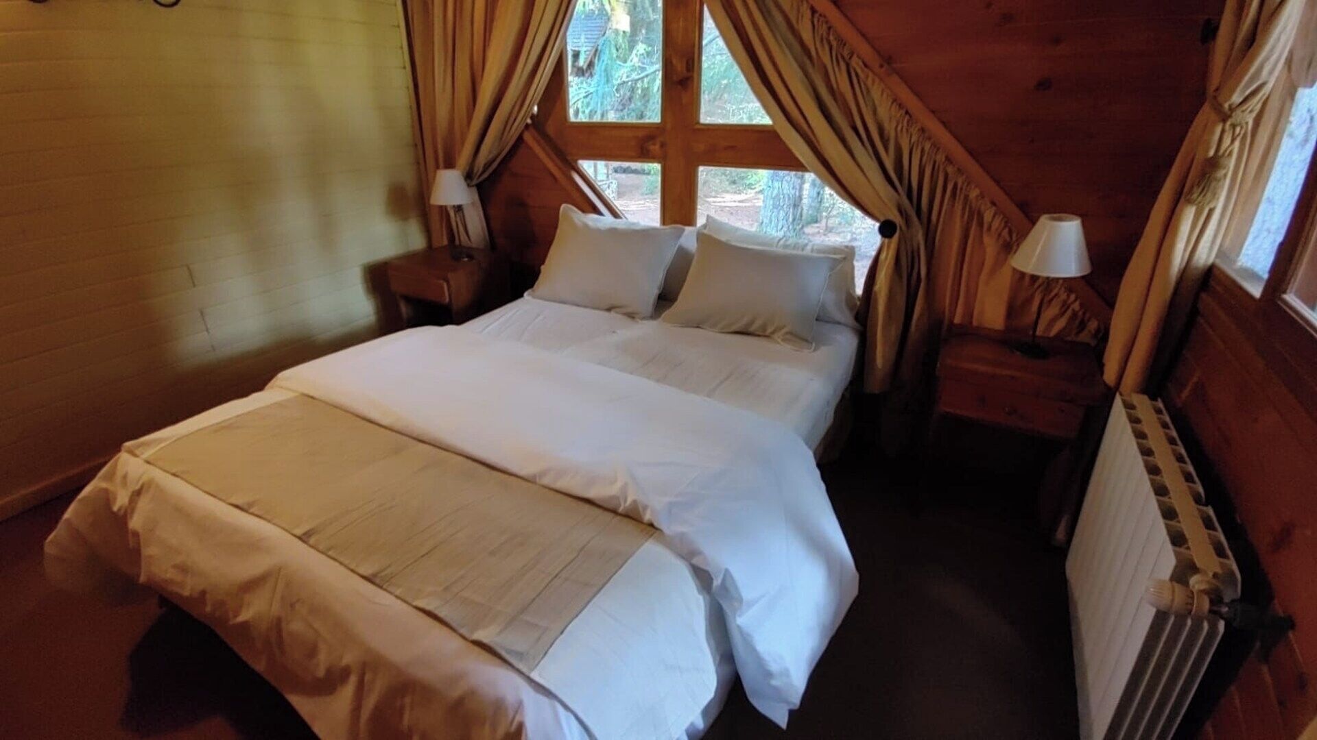 Uma cama de solteiro num quarto com paredes de madeira e uma janela com cortinas.