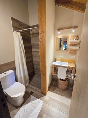 A bathroom with a wooden floor, a white toilet, a shower with a wooden door, a sink with a mirror above it, and a towel rack. - Cabañas en el bosque de Puerto Manzano (Puerto Manzano)