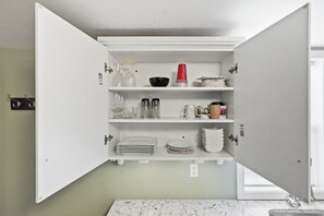Un meuble de cuisine ouvert, avec des étagères contenant de la vaisselle, des verres et une tasse rouge.
