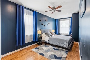 Ein modernes Schlafzimmer mit einem Bett, Nachttischen, einem Deckenventilator und einem geometrischen Teppich.
