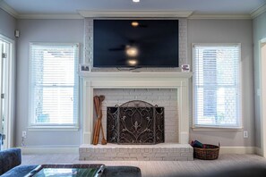 A living room with a fireplace, a television mounted above it, and two windows with blinds. - Lakefront 4BR retreat with deck, kayaks, many dining areas, and cozy fireplace. (Eatonton)