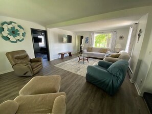 Ein Wohnzimmer mit einem beigen Sofa, einem türkisgrünen Sessel und einem braunen Liegesessel. In der Mitte steht ein Couchtisch und eine Lampe.