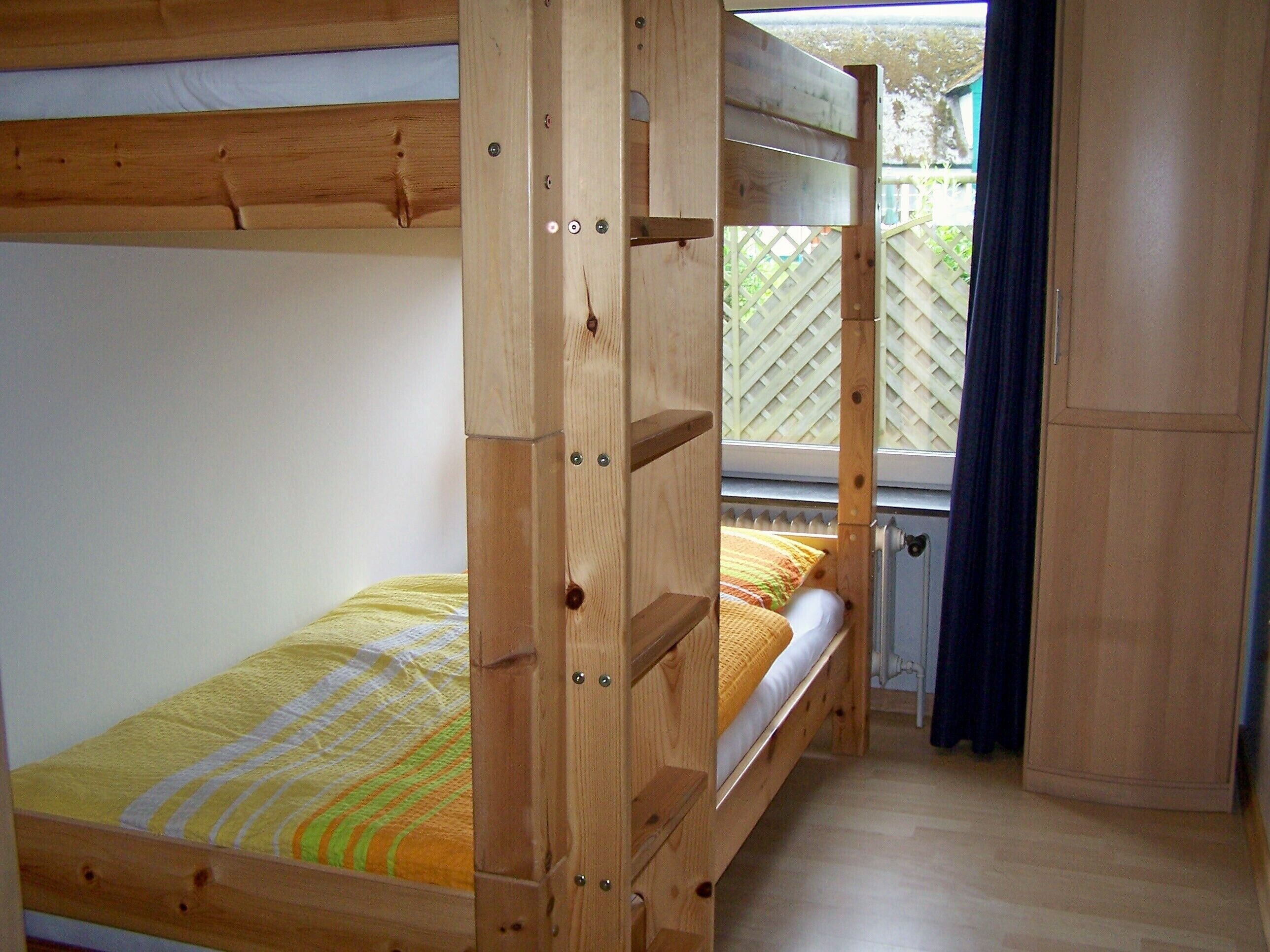 A bunk bed with a wooden frame and a window with a view of a fence.