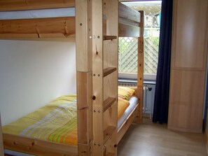 Een stapelbed met houten frame en een raam met uitzicht op een hek.