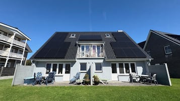 Uma casa de dois andares com varanda, painéis solares no telhado e um pequeno jardim com móveis para área externa.