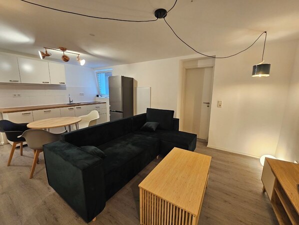 Ein stilvoller Wohnraum mit schwarzem Sofa, Couchtisch aus Holz und einem Essbereich mit Stühlen und Tisch.