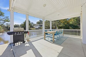 A covered outdoor patio with a grill, a table with chairs, and a view of a lake and trees. - Welcome to Banana Villa,Waterfront,Golf Cart,Kayak,New Home (North Myrtle Beach)