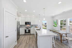 A modern kitchen with white cabinetry, stainless steel appliances, and a large island with bar seating. - Welcome to Banana Villa,Waterfront,Golf Cart,Kayak,New Home (North Myrtle Beach)