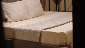 Ein Bett mit einem karopolierten Kopfteil, einer gemusterten Tagesdecke und einem weißen Kissen.