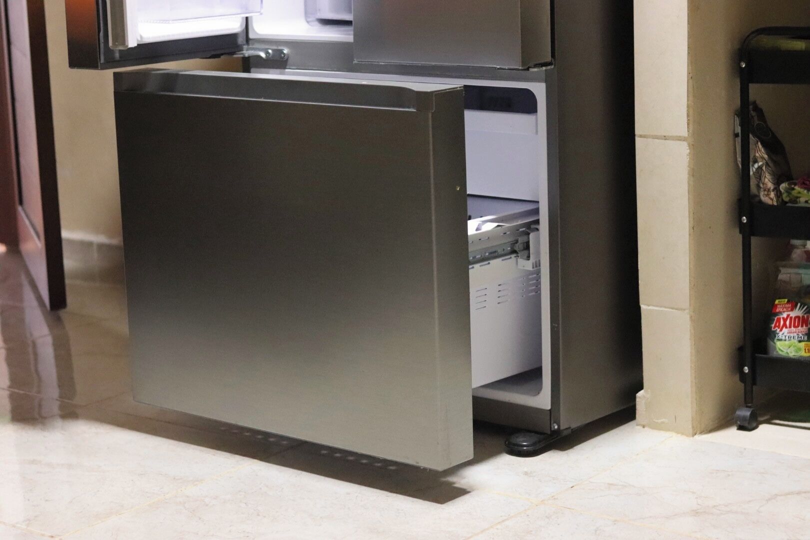 A compact refrigerator with a freezer compartment, situated in a kitchen area with a tiled floor.