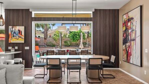 Uma área de refeições moderna com uma grande mesa redonda, várias cadeiras e vista para uma piscina e área externa.