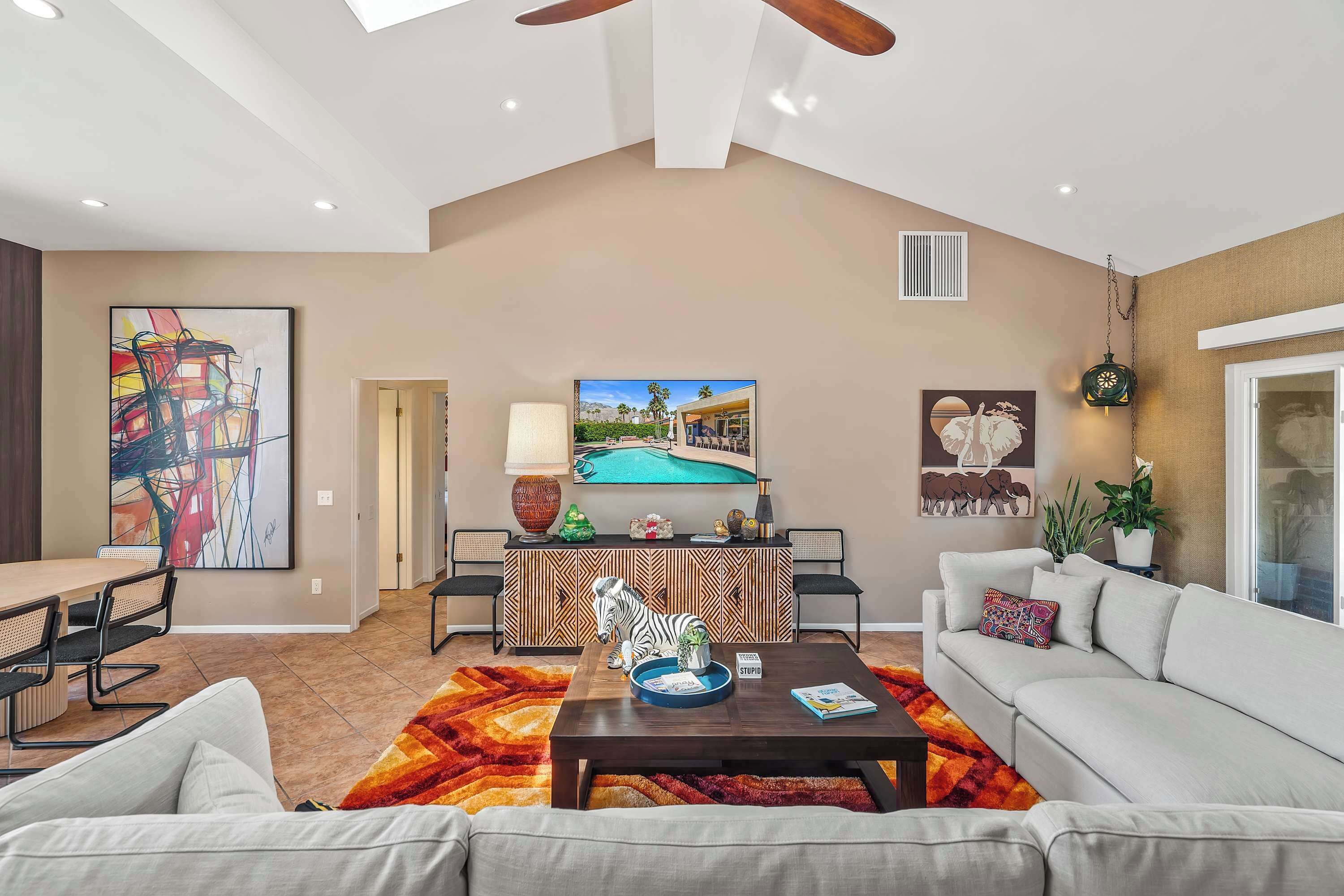 A spacious living room with a high ceiling, a pool view TV, a dining area, and a cozy seating arrangement.