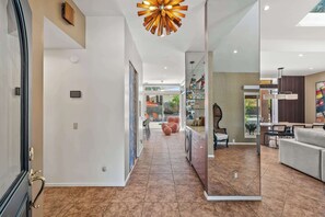 Ein modernes Interieur mit einer Diele, die in einen Essbereich führt, einer Küche mit Glastüren und einem Wohnzimmer mit Sofa und Sesseln.