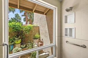 Ein Badezimmer mit Dusche, einem Fenster und Blick auf einen Garten mit Pflanzen und einer Palme.