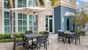 An outdoor patio area with tables and chairs, a large umbrella, and a building with large windows and a stone facade. - Accessible 1 King Studio w/ Hot Breakfast + Pool (St. Petersburg)
