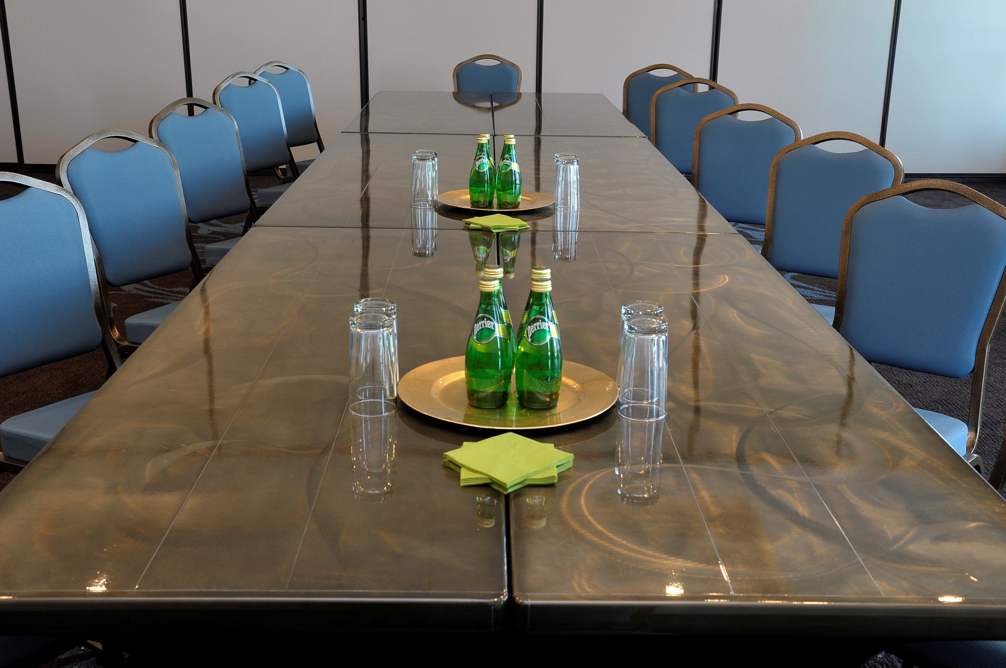 A conference room with a long table, blue chairs, and green bottles on the table.