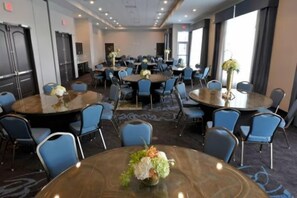 A conference room with multiple tables and chairs, arranged in a U-shape, with large windows on one side.