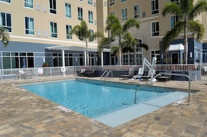 A swimming pool with a tiled deck, surrounded by a white fence, and palm trees. - Two-Queen Studio Suite w/ Daily Breakfast + Pool (St. Petersburg)