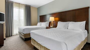 A hotel room with two beds, a television, a lamp, and a large window with curtains.