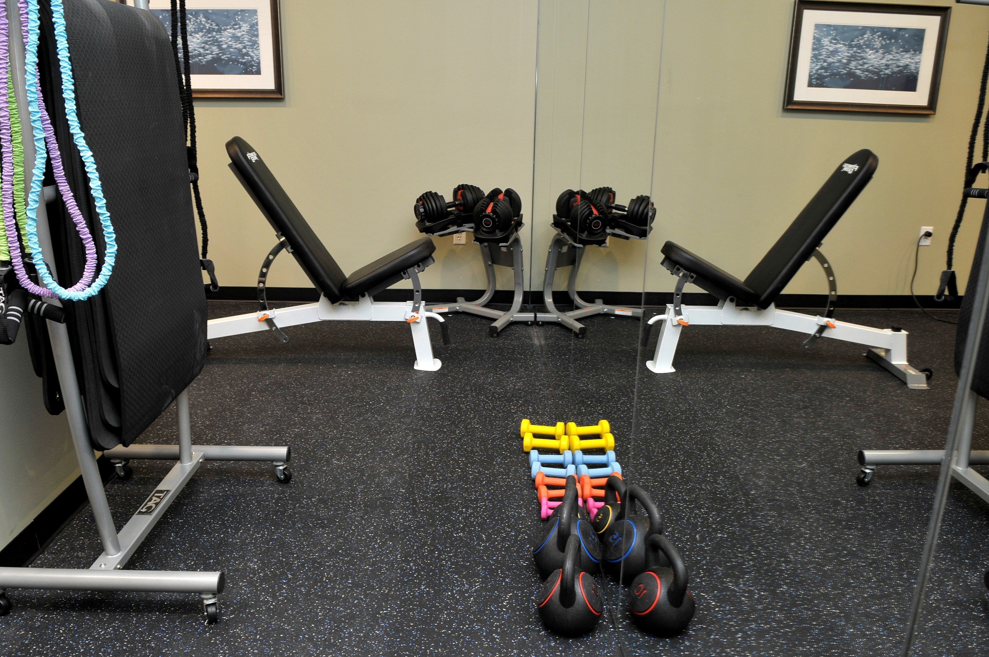 Une salle de sport équipée de matériel de musculation, de bancs et d’un miroir.