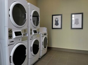 A laundry facility with multiple stacked washing machines and two framed pictures on the wall.