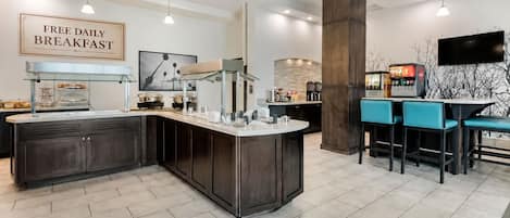 A modern kitchen with a free daily breakfast sign, a central island, bar seating, and a large pillar.