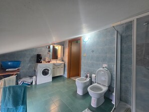 A compact bathroom with a washing machine, two toilets, a sink, and a shower area. - Vrbo Property (Riposto)