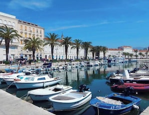 A marina with boats docked, palm trees, and buildings in the background. - The Heart of Old Town (Split)
