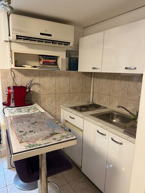 A kitchen with white cabinets, a stove, a sink, and a red kettle. - The Heart of Old Town (Split)