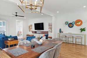 A modern living room with a wooden dining table, blue sofas, and a ceiling fan. - 4BR Escape for 12, East Nash Walkable Location! (Nashville)