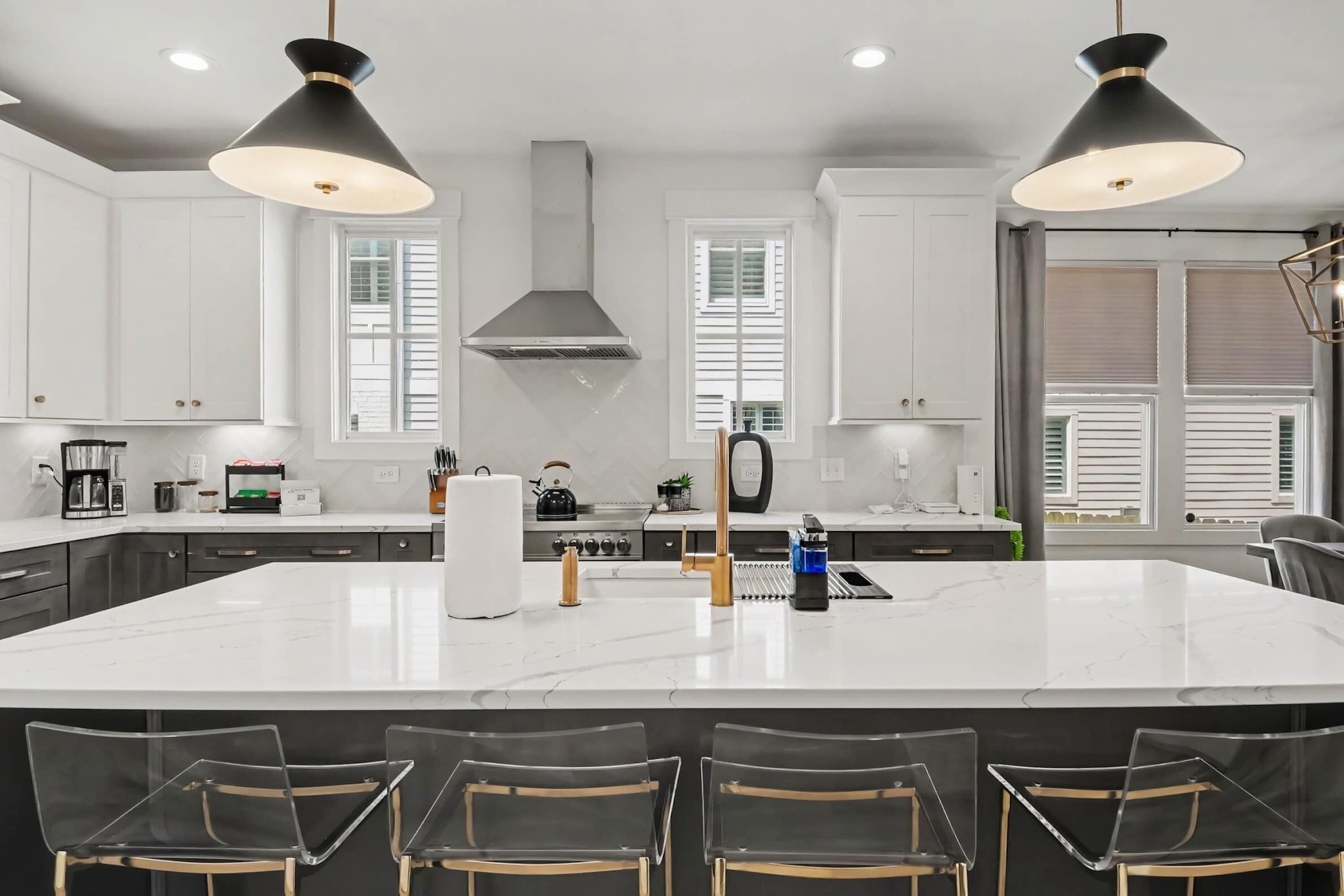 A modern kitchen with a large island, white cabinets, stainless steel appliances, and pendant lighting.