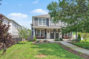 A two-story residential house with a front porch, a small garden, and a visible mailbox. - 4BR Escape for 12, East Nash Walkable Location! (Nashville)