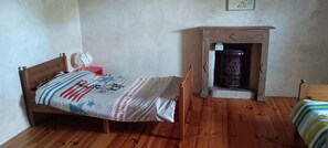 A room with a wooden bed, a small fireplace, and a plain wall. - Charming stone house with a garden – Finistère, near the sea (Quéménéven)