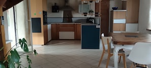 A modern kitchen with a central island, wooden cabinets, and a dining area with a table and chairs. - Charming stone house with a garden – Finistère, near the sea (Quéménéven)