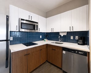 A modern kitchen with white cabinets, a stainless steel microwave, a dishwasher, and a coffee maker.