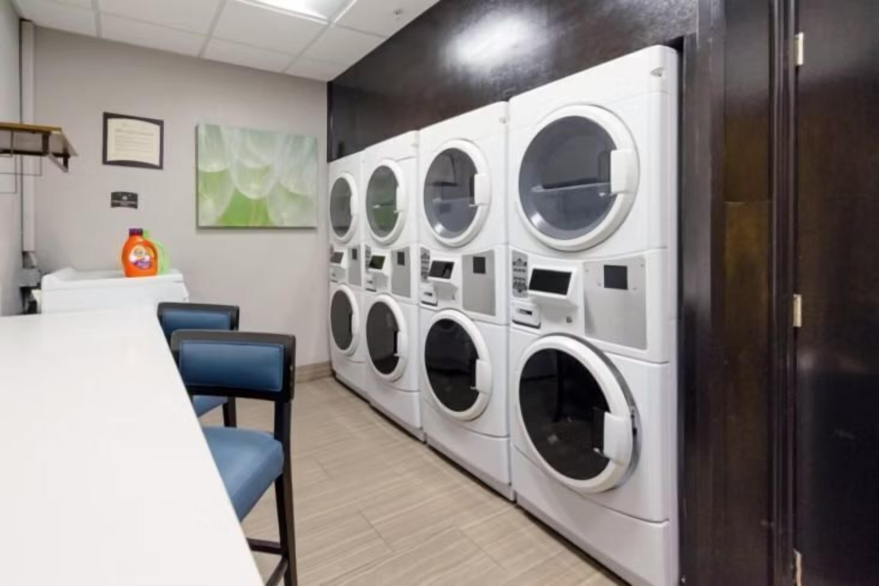 A laundry area with multiple washing machines, a table, chairs, and a wall-mounted fire extinguisher.