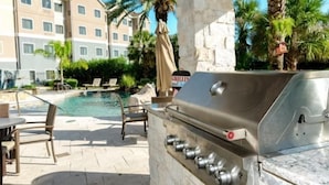 An outdoor pool area with a grill and lounge chairs.